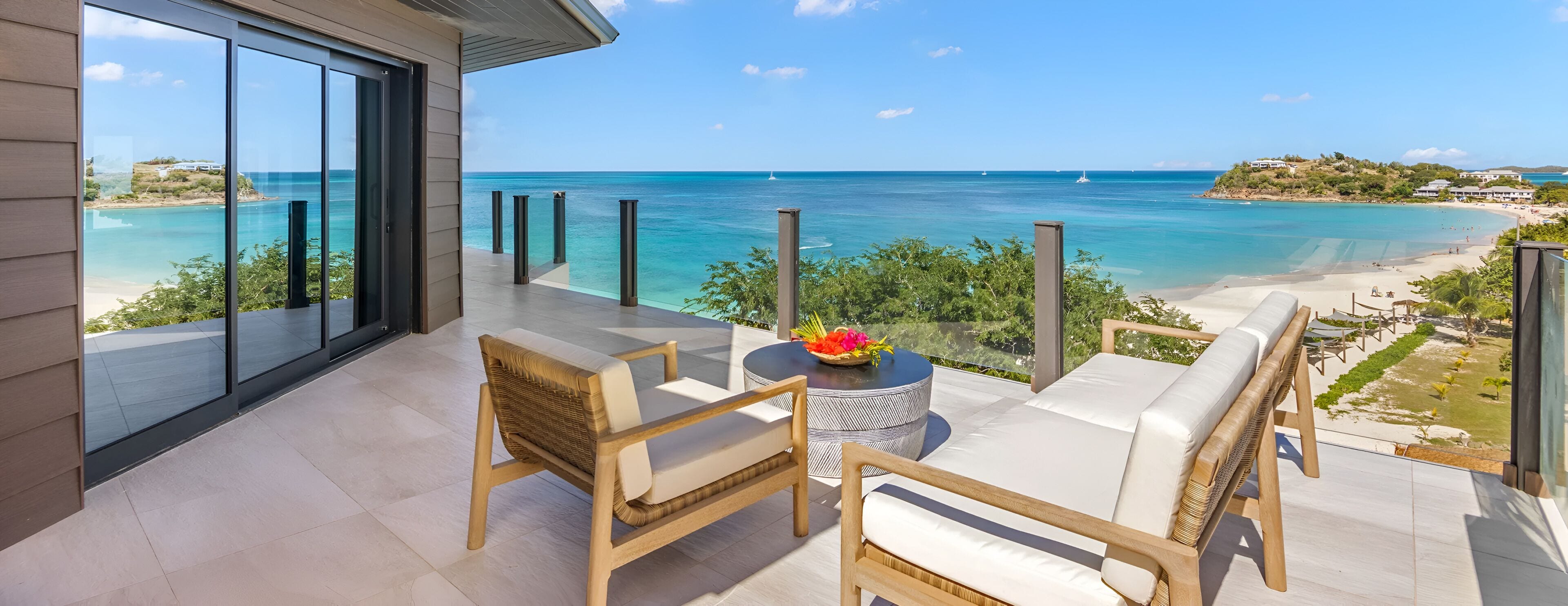 Ein Balkon mit Blick auf Strand und Meer, ausgestattet mit Korbstühlen und einem Tisch mit Blumen.