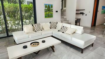 A modern living room with a white sectional sofa, a white coffee table, and a painting of a tropical landscape.
