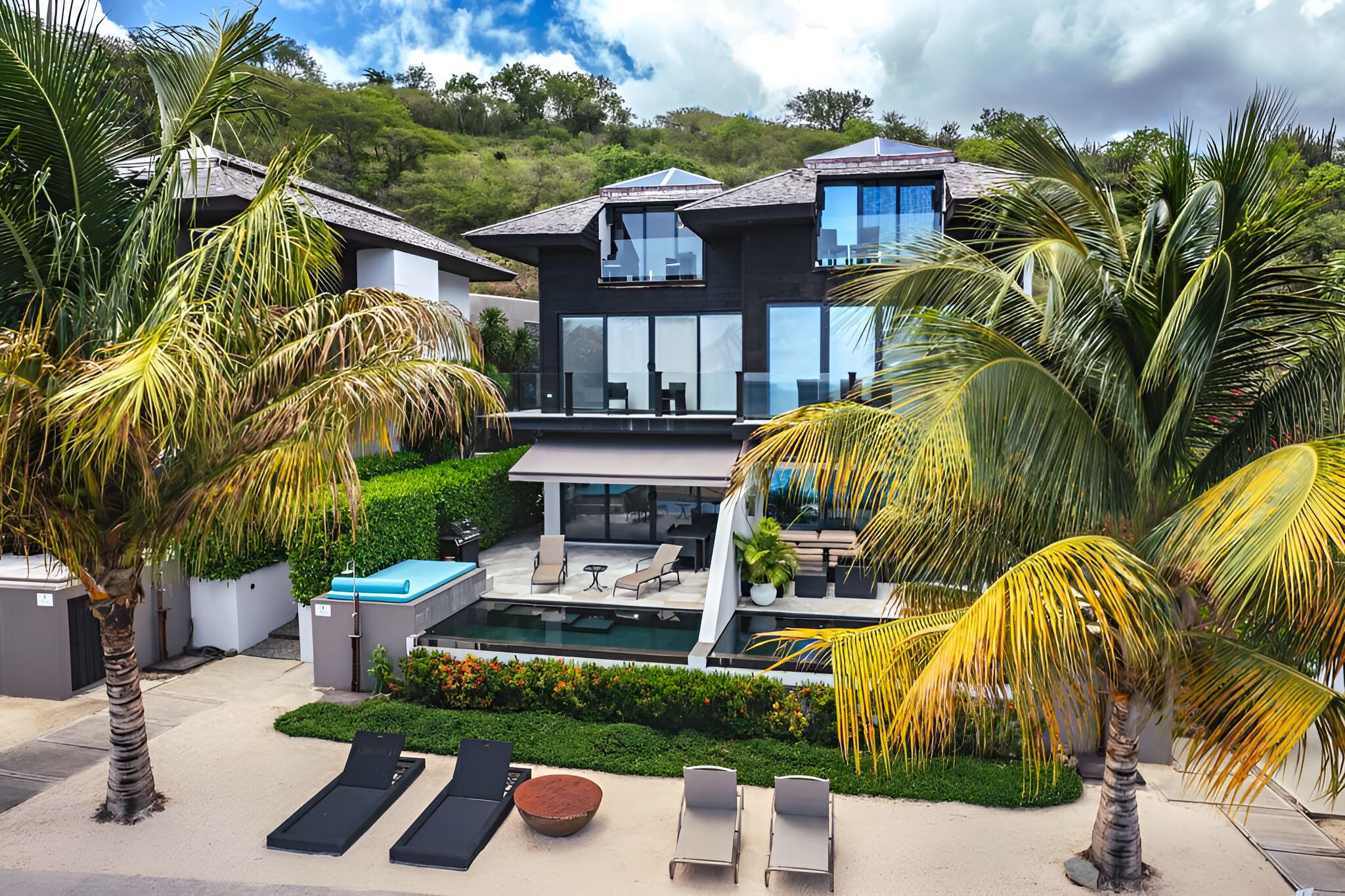 A modern house with a swimming pool, lounge chairs, and palm trees.