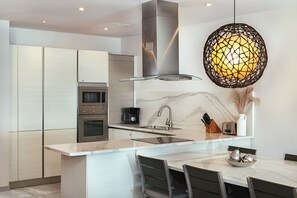 A modern kitchen with a central island, stainless steel appliances, and a unique pendant light.