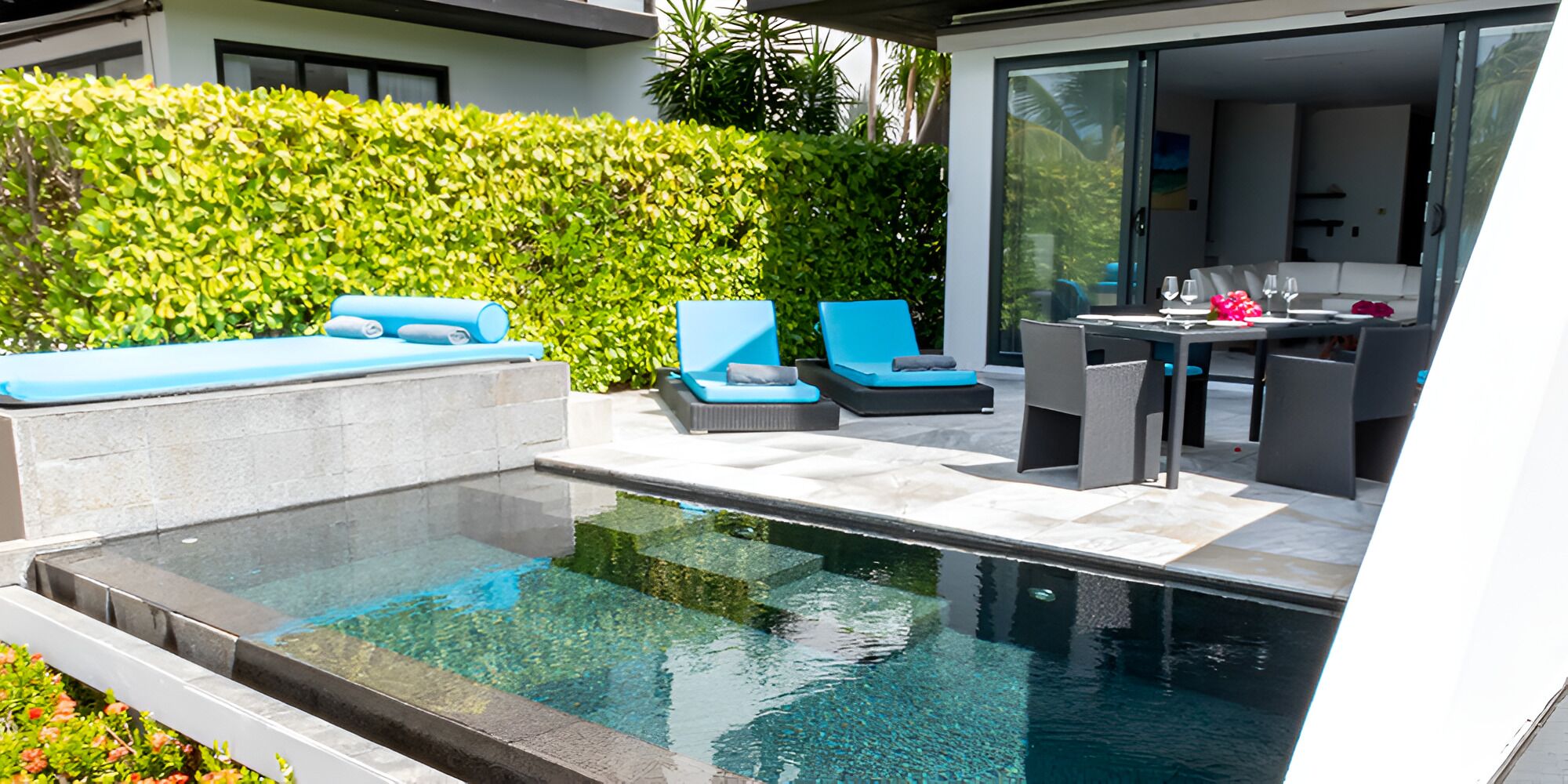 A modern outdoor pool area with a clear pool, blue lounge chairs, and a dining table with chairs.