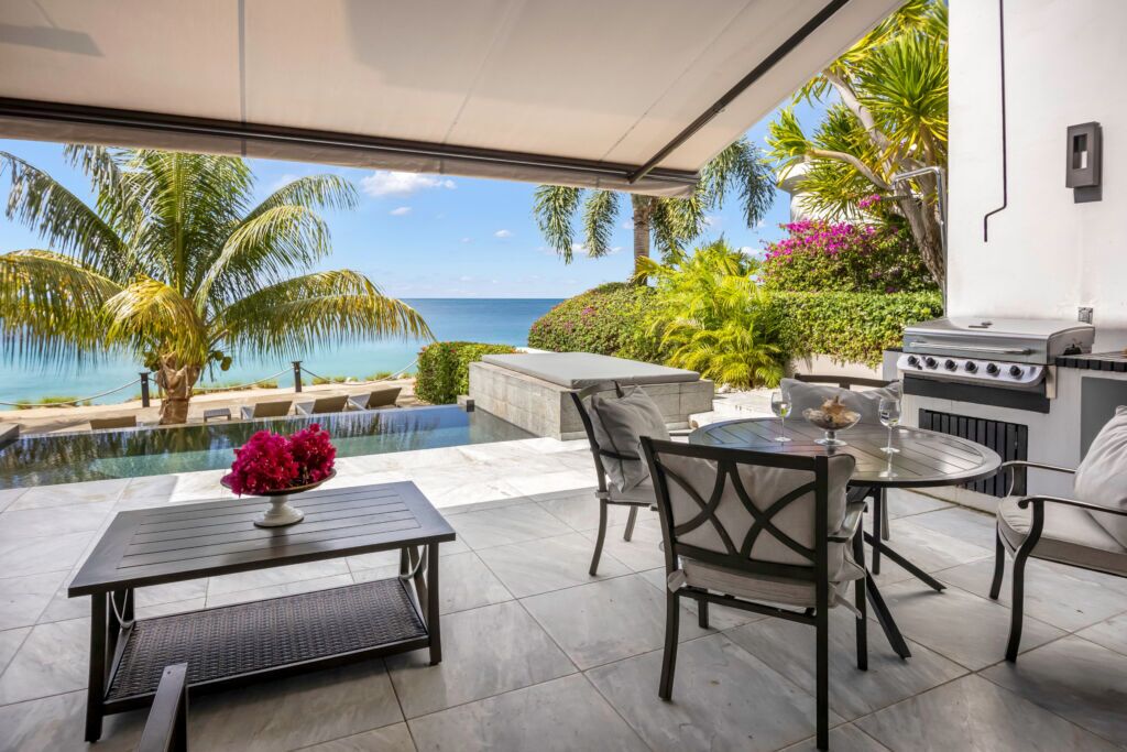 An outdoor patio with a view of the ocean, a grill, and a pool.