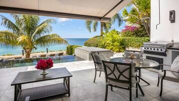 An outdoor patio with a view of the ocean, a grill, and a pool.