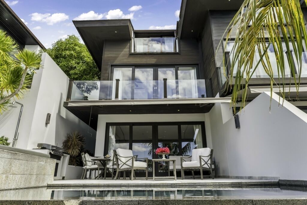 Ein modernes, zweistöckiges Haus mit Balkon, Sitzgelegenheit im Freien und einem Pool.