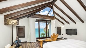 Une chambre avec un grand lit, une télévision, un banc en bois et une vue sur l’océan.