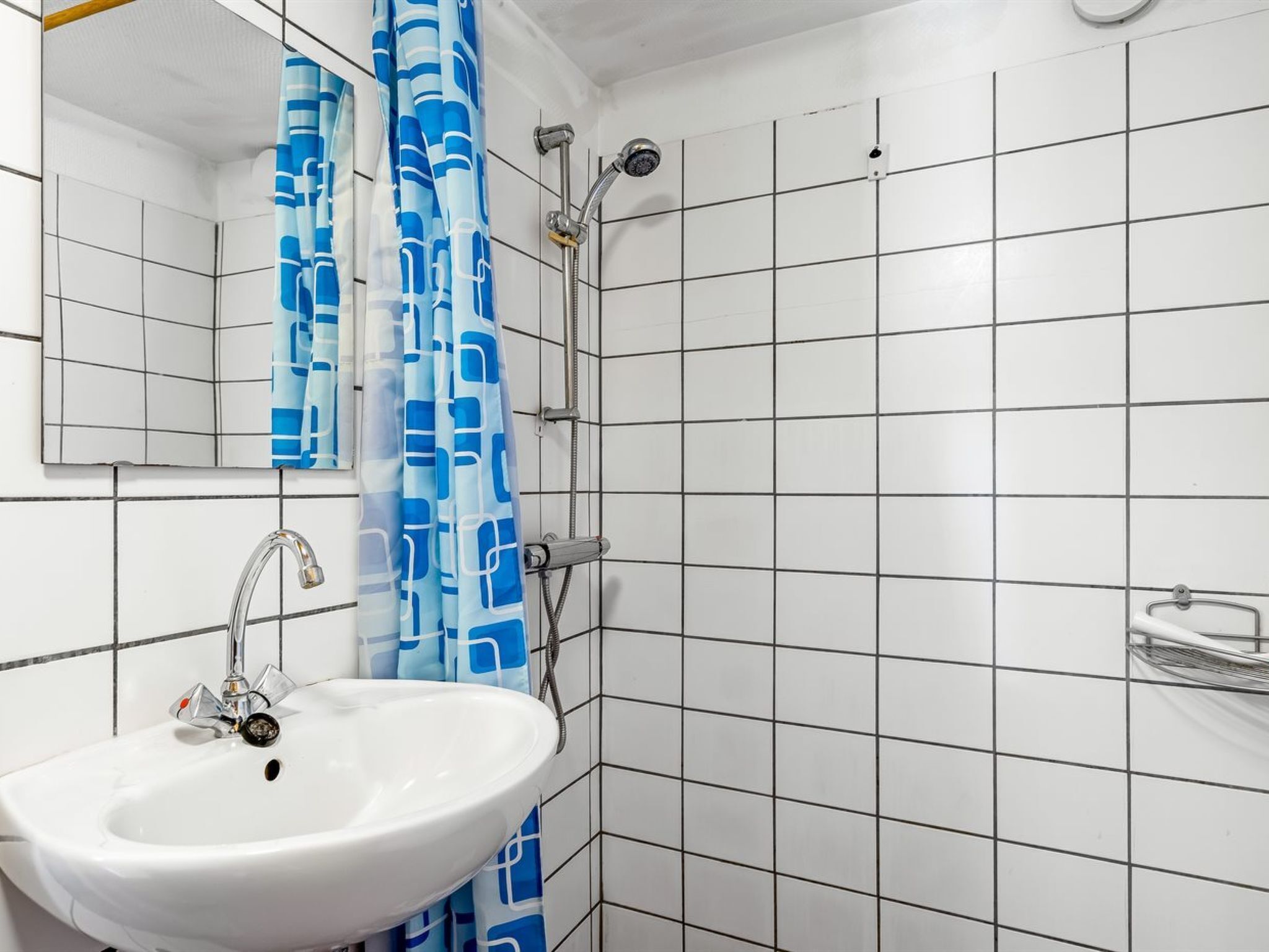 A bathroom with a white sink, a mirror, a shower with a blue curtain, and tiled walls.