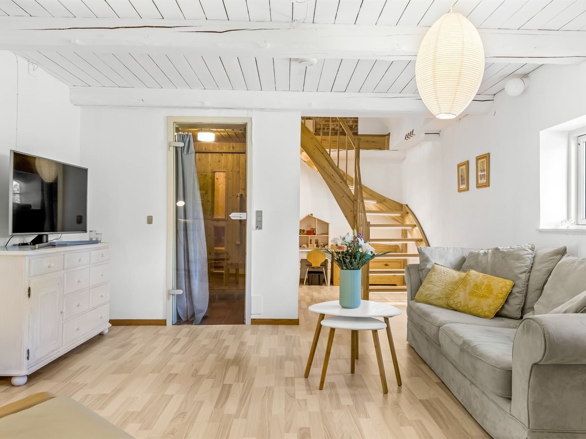 A modern living room with a grey sofa, a white TV stand, and a wooden staircase leading to an upper level.