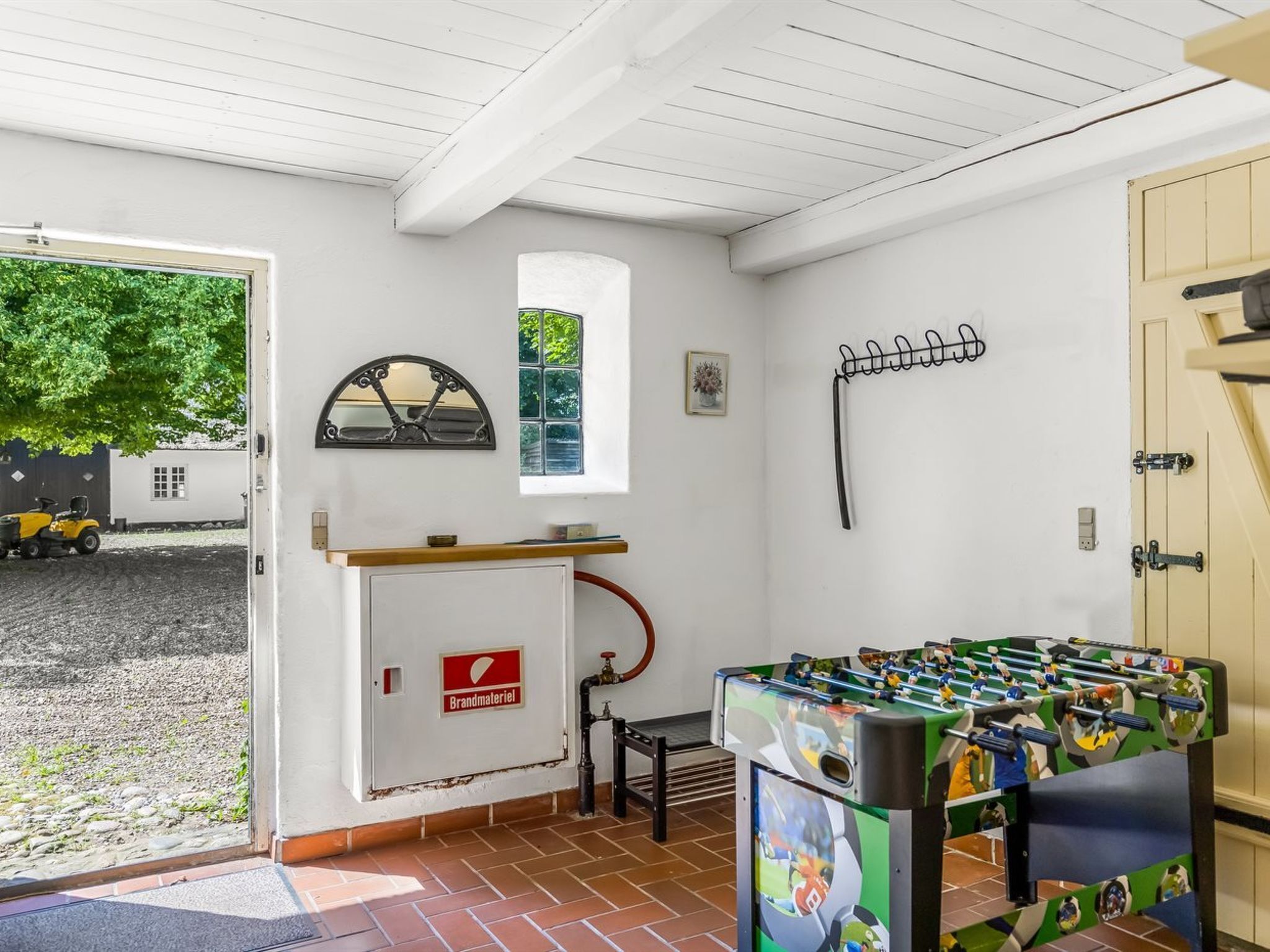 Una habitación con mesa de fútbolín, extintor Brandmayer, una ventana y una puerta.