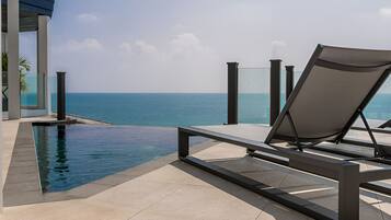 A modern poolside area with a clear view of the ocean, a lounge chair, and a glass-enclosed structure.