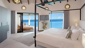 Un dormitorio moderno con una cama grande, un balcón con vistas al mar e iluminación geométrica en el techo.
