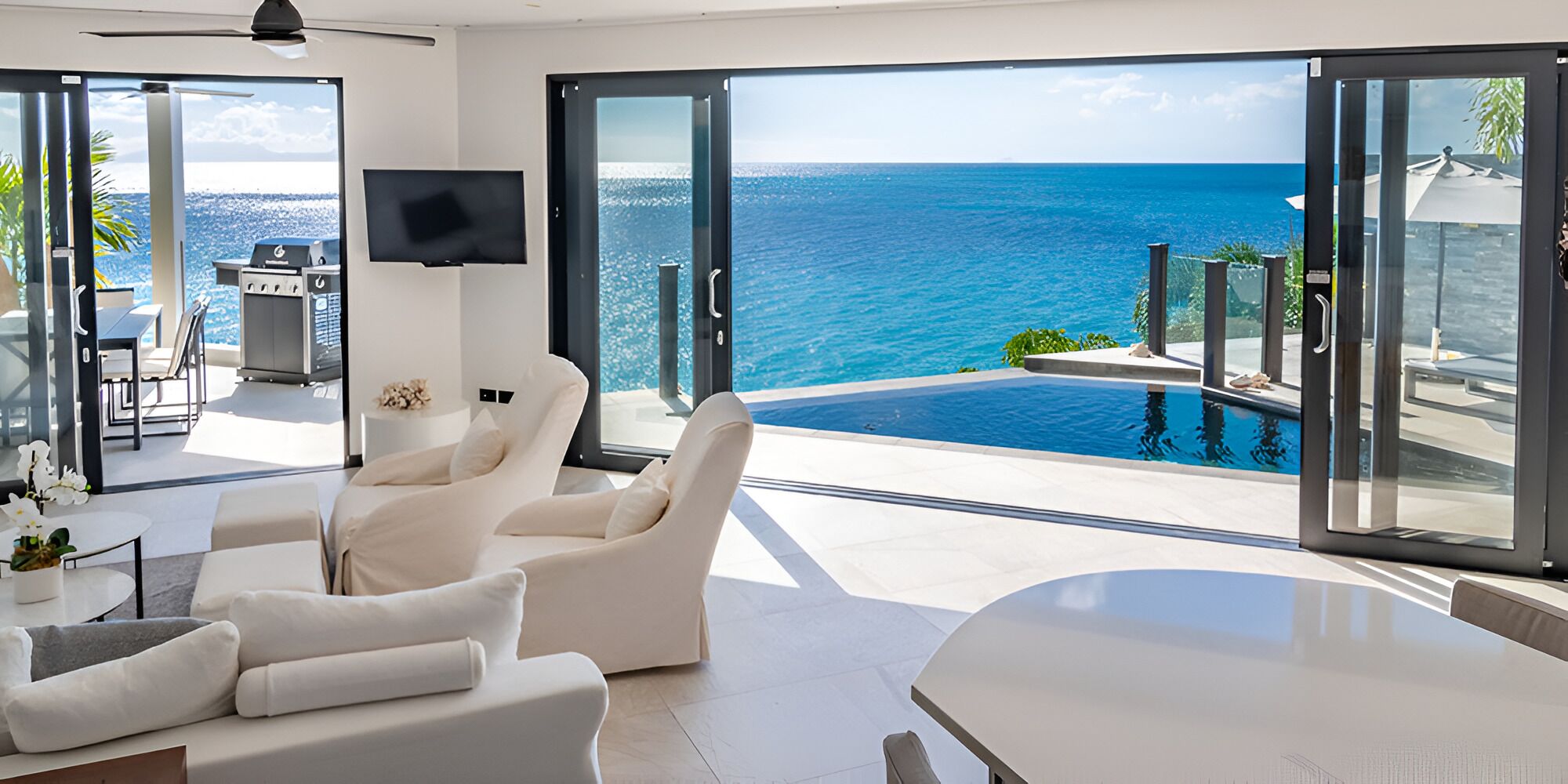 A modern living room with a large sliding glass door leading to a pool overlooking the ocean.