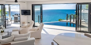 Una sala de estar moderna con un amplio ventanal corredera que da a una piscina con vista al océano.