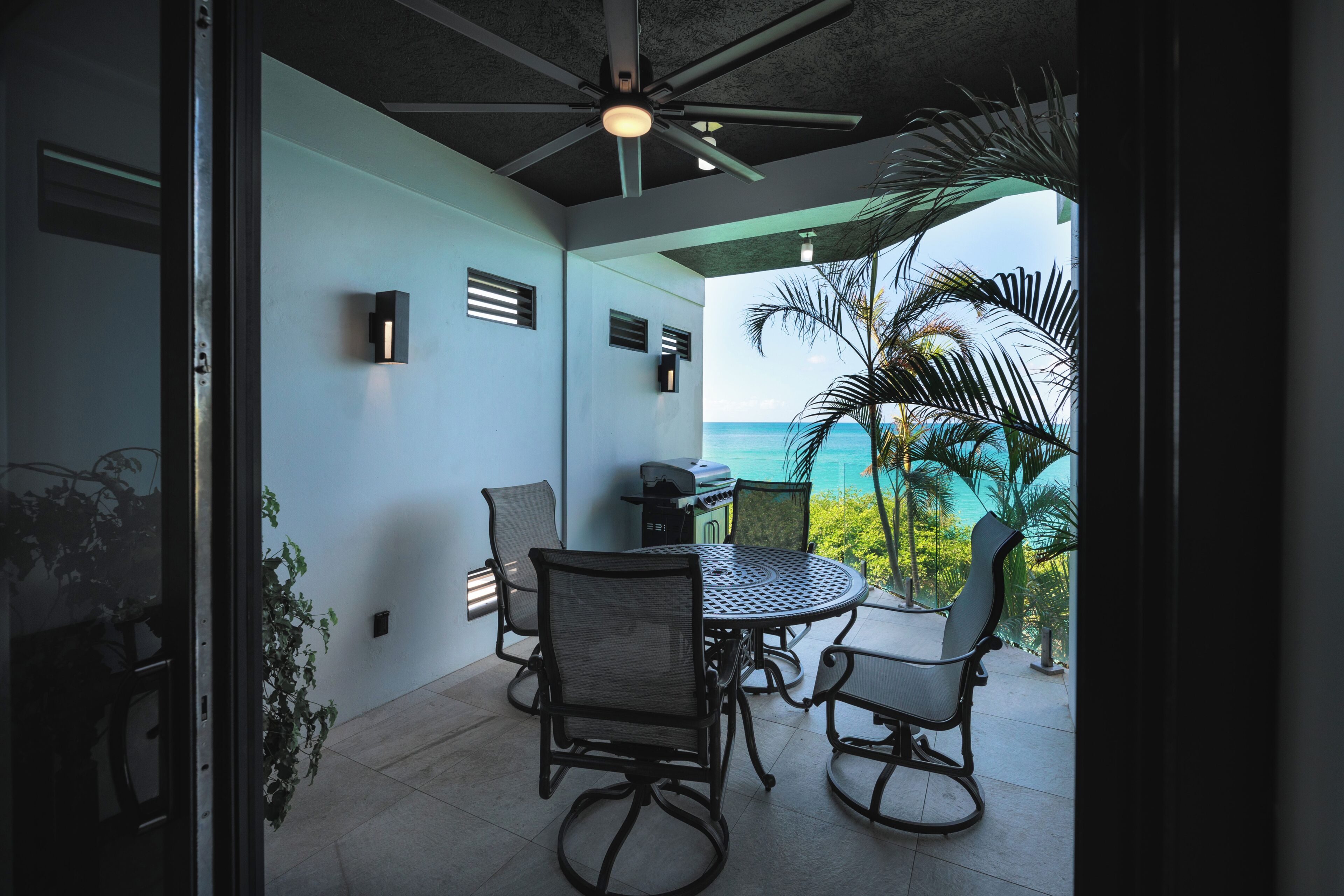 Eine Terrasse mit rundem Tisch und Stühlen, einem Deckenventilator und Blick aufs Meer.
