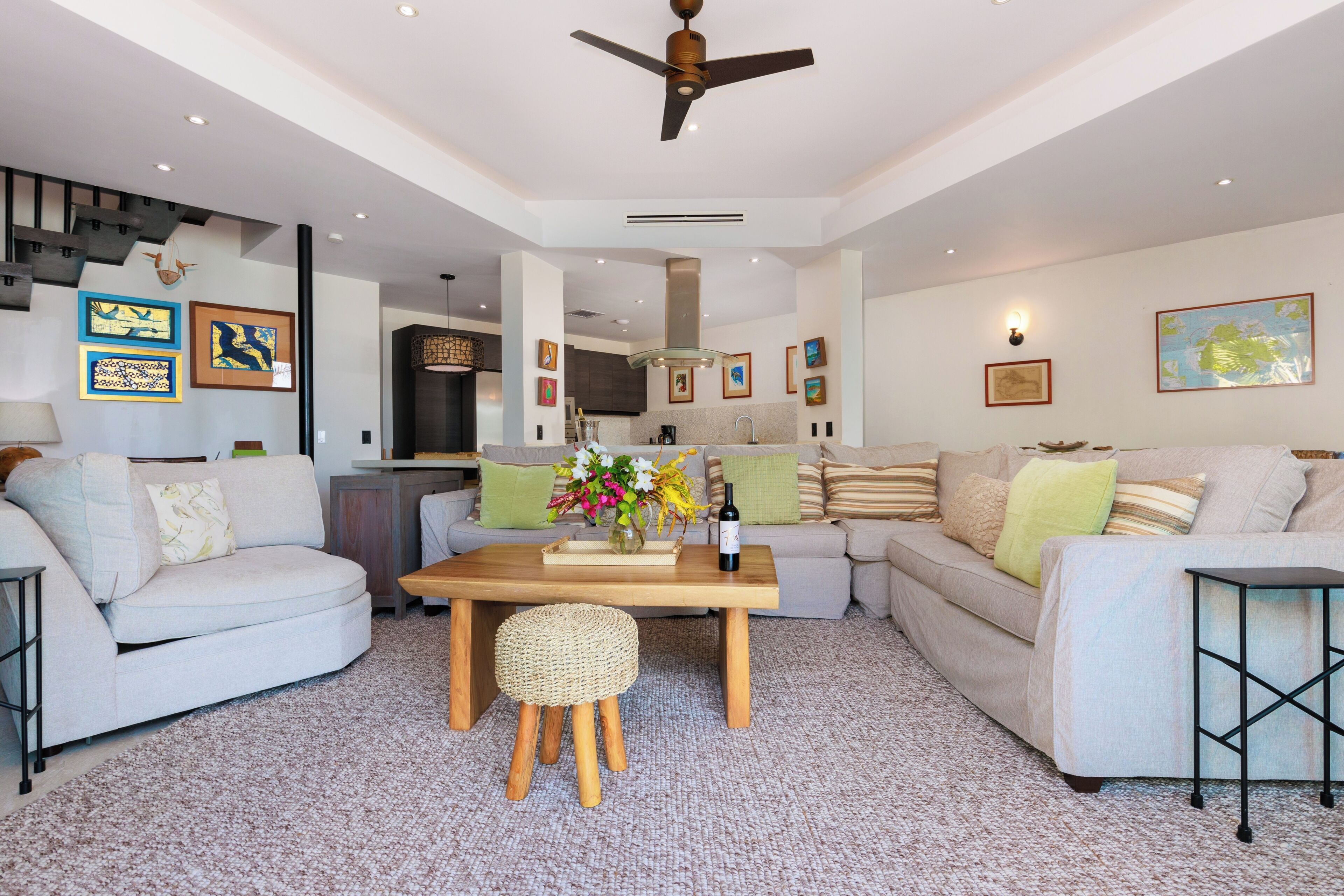 Ein geräumiges Wohnzimmer mit einer Couch, einem Couchtisch und einem Essbereich. Ein Deckenventilator ist sichtbar, und Kunstwerke sind an den Wänden ausgestellt.
