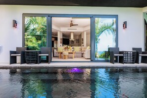 Un área moderna junto a la piscina con zona de comedor y vistas al interior.