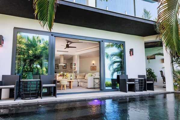 Una casa moderna con piscina, grandes puertas correderas de vidrio y mobiliario exterior.