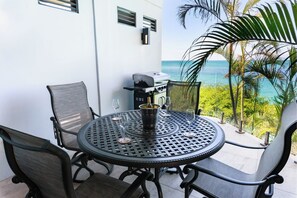 A round metal table with four chairs, a grill, and a wine bucket on a balcony overlooking the ocean. - Oasis: Luxury 2-Bedroom Villa with Boardwalk to Darkwood & Ffryes Beach, Antigua (Urlings)