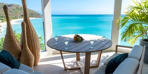 Mesa redonda con frutero y copas de vino, con vista a una playa y al océano.