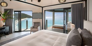 Una habitación de hotel moderna con una cama grande, un escritorio y una silla. La habitación tiene ventanas amplias que ofrecen vistas a la playa y al océano.