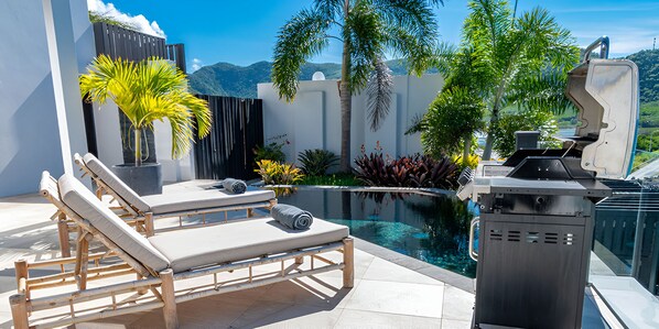 Un área de piscina en la azotea con sillones de descanso, una parrilla y varias plantas.