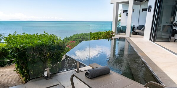 A modern infinity pool with a clear view of the ocean, surrounded by lush greenery and a contemporary outdoor seating area. - Oceanview Villa with Infinity Pool & Direct Beach Access (Urlings)