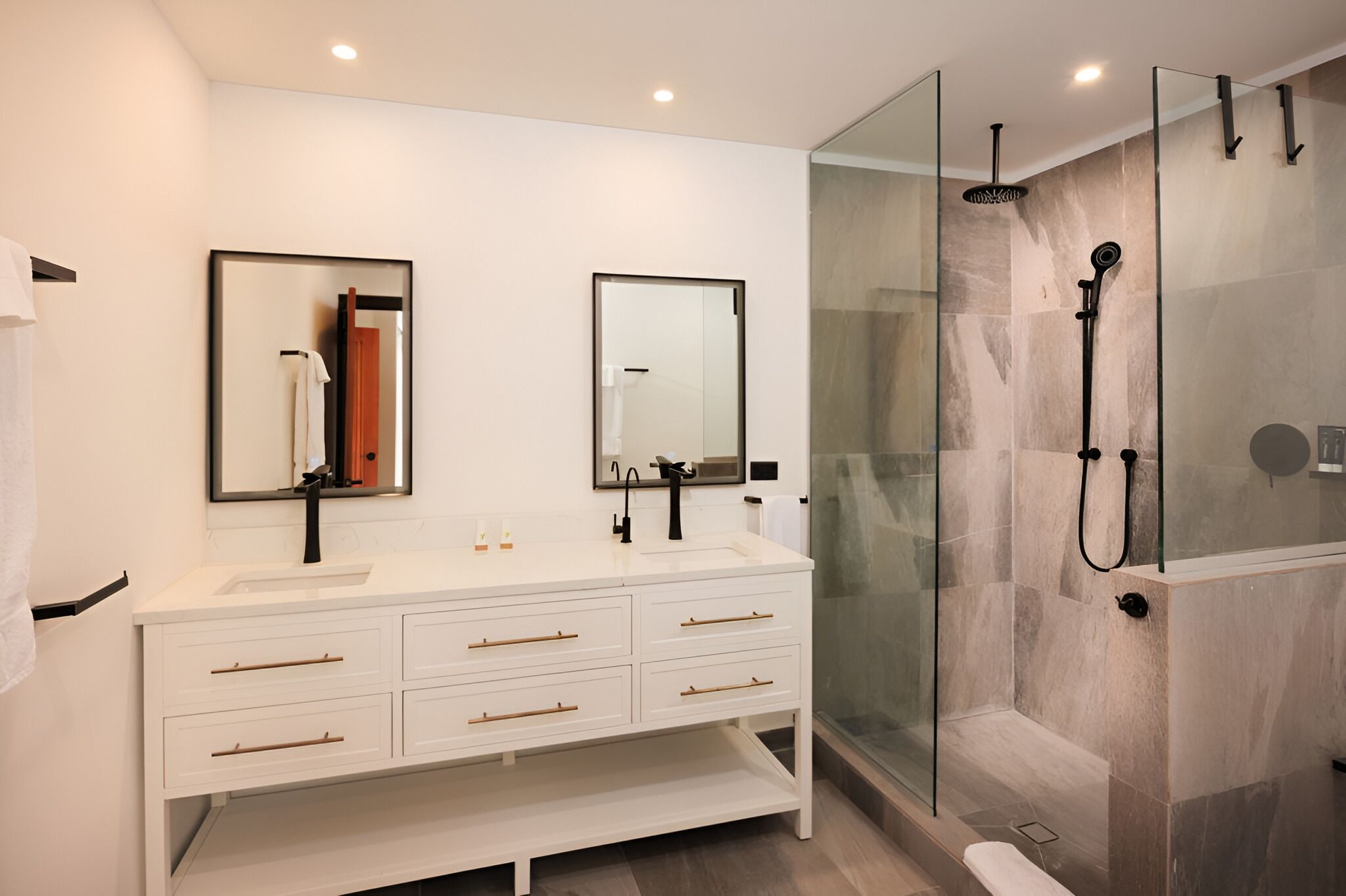 A modern bathroom with a white vanity, two mirrors, a glass shower enclosure, and a white sink.