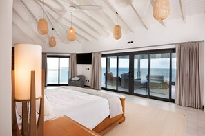 Un dormitorio moderno con una cama grande, suelo de madera y vistas al mar a través de puertas de cristal amplias.