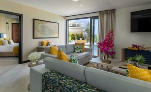 A modern living room with a sofa, a coffee table, and a TV. There is a window with a view of the outside.
