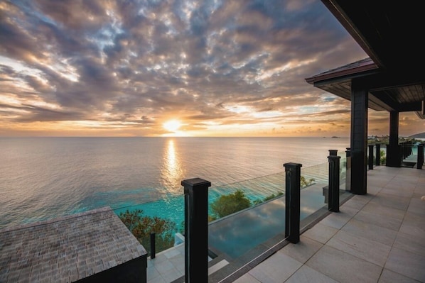 Vista al atardecer desde un balcón con piscina, con vista al mar.