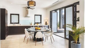 Une cuisine moderne avec un coin repas, comprenant une table ronde pour six personnes, des meubles de rangement aux couleurs sombres et une grande fenêtre offrant une vue dégagée.