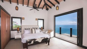 Une chambre à coucher avec un lit, des tables de chevet et une vue sur l’océan.