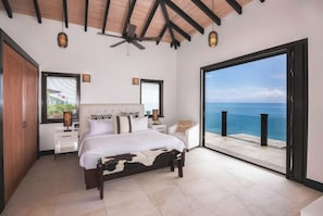 Un dormitorio con una cama grande, un ventilador de techo y vista al océano.