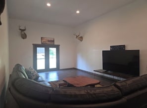 A living room with a leather sofa, a flat-screen TV, and two mounted deer heads. - Lovely 3-bedroom newly constructed barndominium perfect for relaxing stays. (Baldwin)