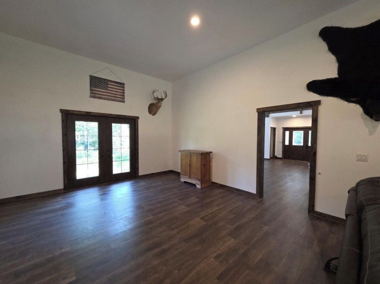 Une pièce spacieuse avec un plancher en bois foncé, une armoire en bois, un drapeau américain et une tête de cerf montée au mur.