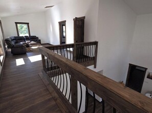 A spacious living area with a dark wooden floor, a wooden railing, and a sectional sofa.