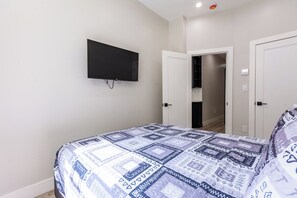 A bedroom with a bed, a TV mounted on the wall, and a door leading to a closet.