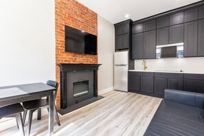 A modern kitchen with a brick wall, a flat-screen TV, dark cabinets, and a built-in microwave.