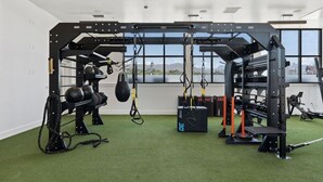 Ein Fitnessraum mit Krafttrainingsgeräten, einem Boxsack und Blick auf eine Stadtlandschaft durch große Fenster.