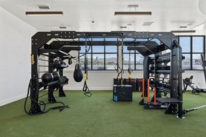 Ein Fitnessraum mit Krafttrainingsgeräten, einem Boxsack und Blick auf eine Stadtlandschaft durch große Fenster.