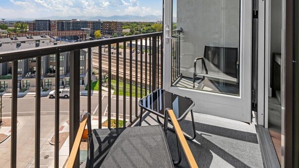 Ein Balkon mit Metallgeländer, einer Glastür und Blick auf einen Parkplatz und Gebäude.