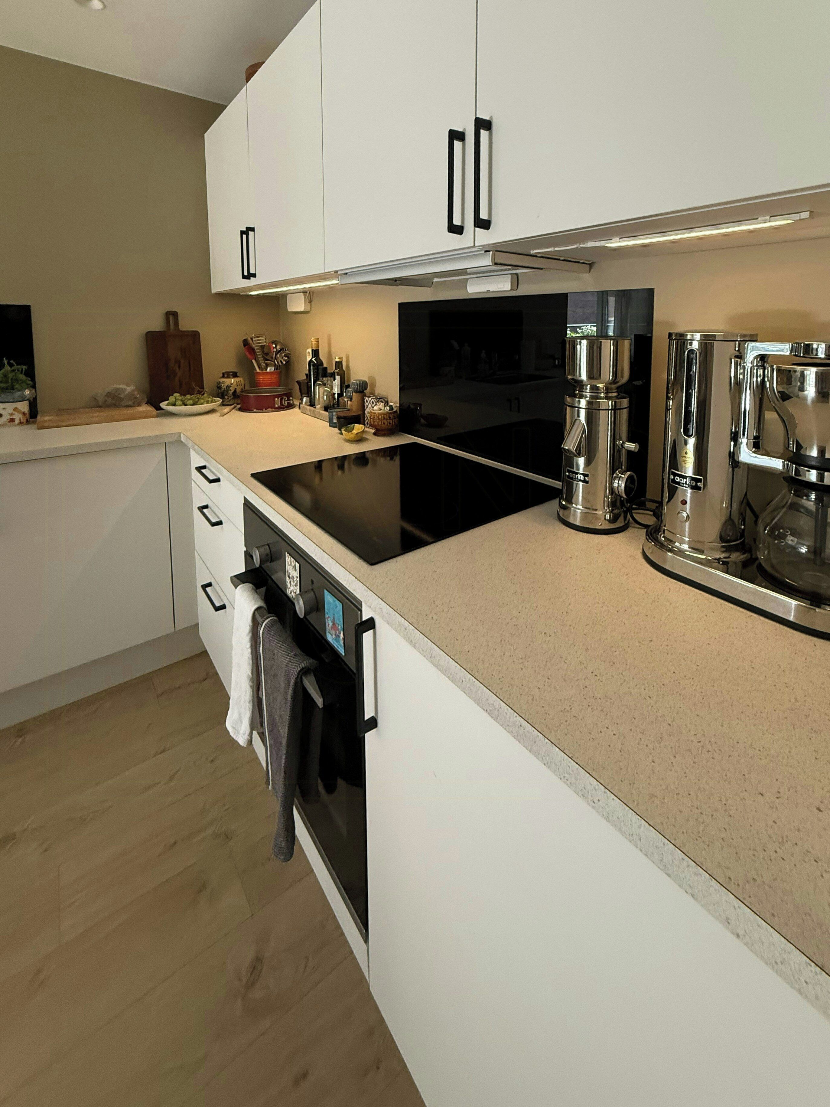 Una cucina moderna con mobili bianchi, un piano cottura nero ed elettrodomestici in acciaio inossidabile.