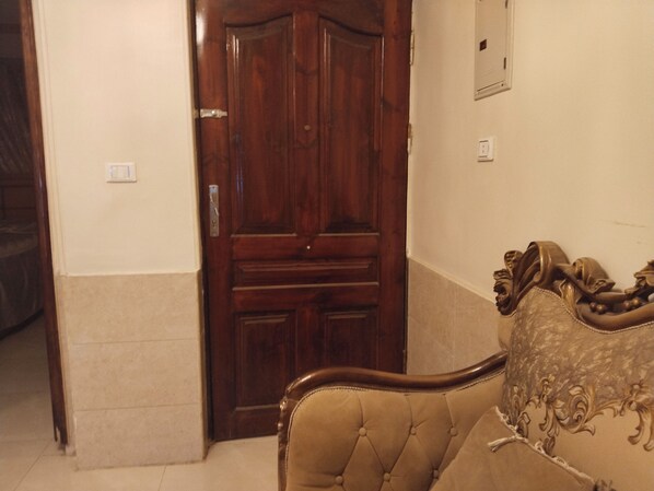 Una habitación con puerta de madera, un interruptor de luz y una cama con cubrecolcha estampada.