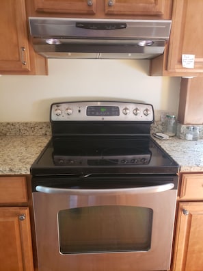 Un horno de acero inoxidable con panel de control digital, una campana extractora encima y armarios de madera.