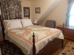 Um quarto com uma cama de madeira, um edredom, uma mesa de cabeceira, uma cadeira e uma janela com cortinas.
