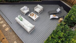 A deck with a sofa, two armchairs, and a table with a tray of food and drinks. - Acacia Mollymook Beach | Pool & Tennis Court (Mollymook Beach)