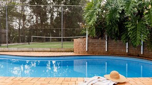 Ein Swimmingpool mit Ziegelbordstein, einem Zaun und einem Baum im Hintergrund.
