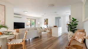 Ein großzügiger Wohnbereich mit einer Couch, einem Esstisch und Stühlen, eine Küchenzeile mit einem Esstisch sowie ein großes Fenster für natürliches Licht.
