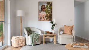A modern living room with a sofa, armchair, and a small table with decorative items. - Acacia Mollymook Beach | Pool & Tennis Court (Mollymook Beach)