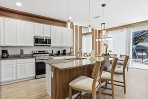 A modern kitchen with white cabinets, stainless steel appliances, and a central island with chairs. - Disney 6BR/4BA Themed Rooms & Pool LED TV BV4509 (Kissimmee)