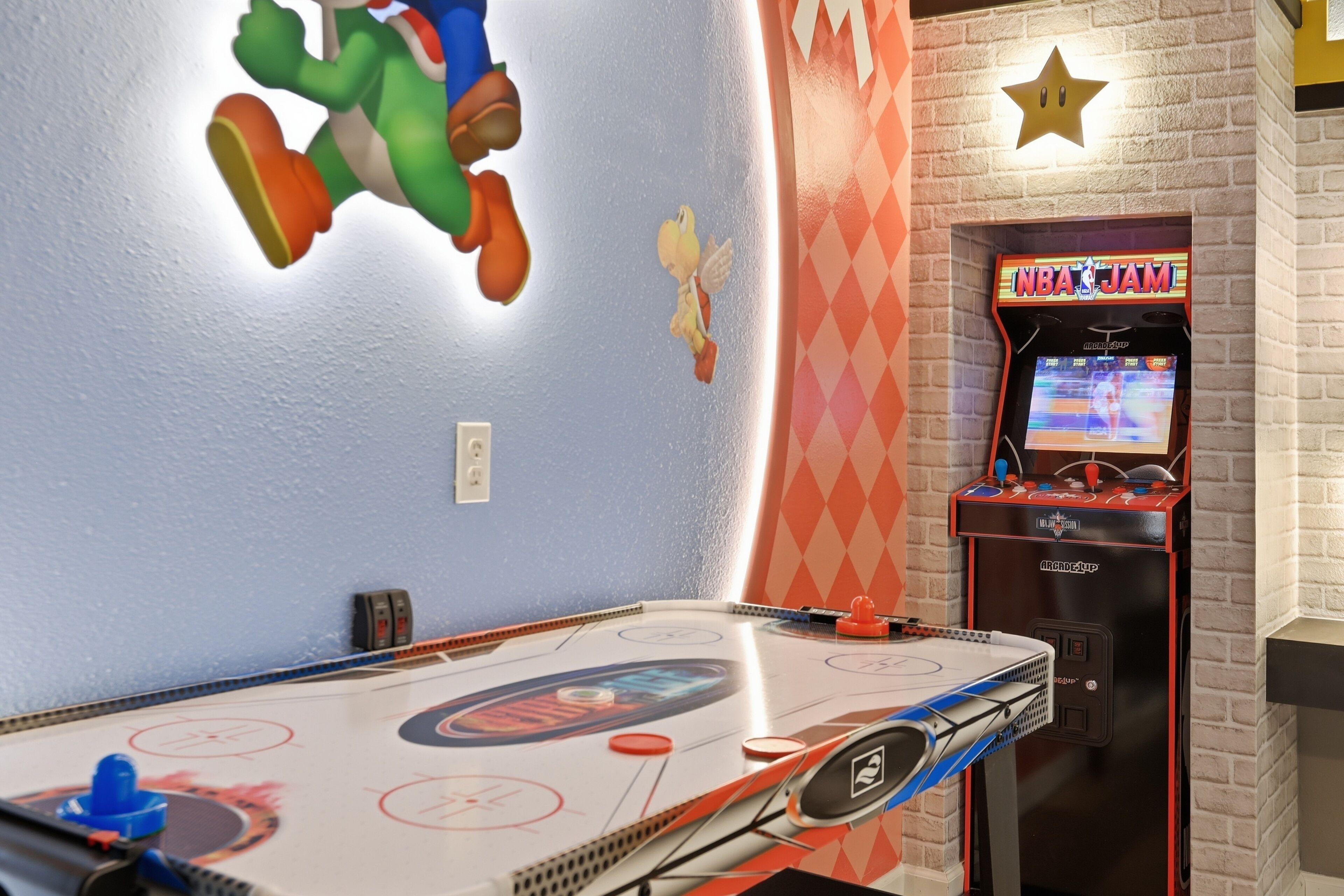 Una habitación con mesa de futbolín, máquina recreativa de Nintendo 64 y una pared decorada con un personaje de Mario.